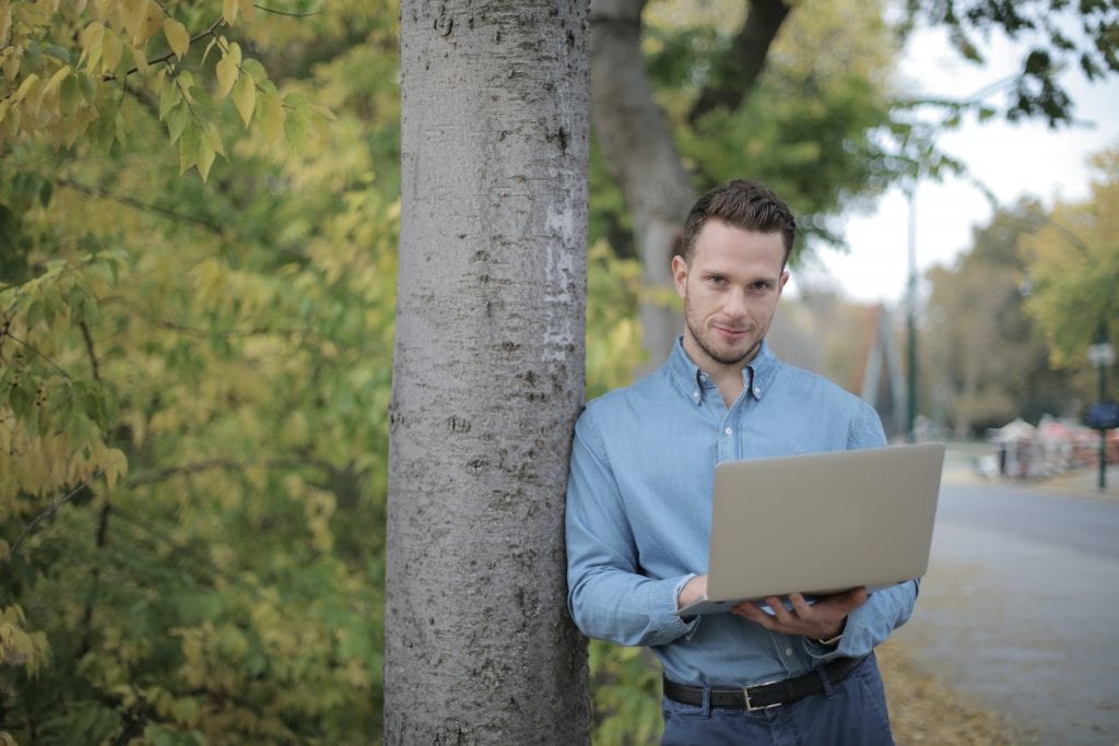 positive-young-man-using-laptop-near-tree-in-park-3973338