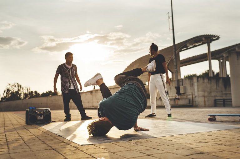 Young Male Performing A Dance Pose In The Park At Sunset Surrounded By Mixed Race Group Of Friends