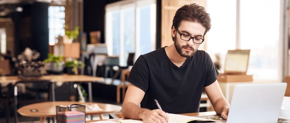 Freelancer,Bearded,Man,In,T-shirt,Taking,Notes,At,Laptop,Sitting